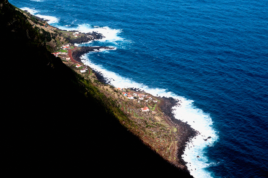 Elevated view of a narrow faj&atilde; on S&atilde;o Jorge Island, with red-roofed houses and small agricultural plots extending along the rocky Atlantic shoreline.