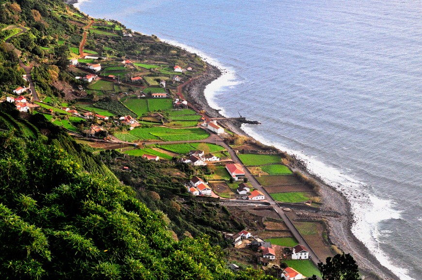 Traditional coastal faj&atilde; on S&atilde;o Jorge Island with cultivated fields, white houses with red roofs and a narrow road running beside the Atlantic Ocean.