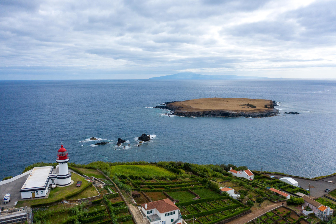 Ponta do Topo Lighthouse on the eastern coast of S&atilde;o Jorge Island overlooking Ilh&eacute;u do Topo and the Atlantic Ocean, with cultivated fields surrounding the headland.