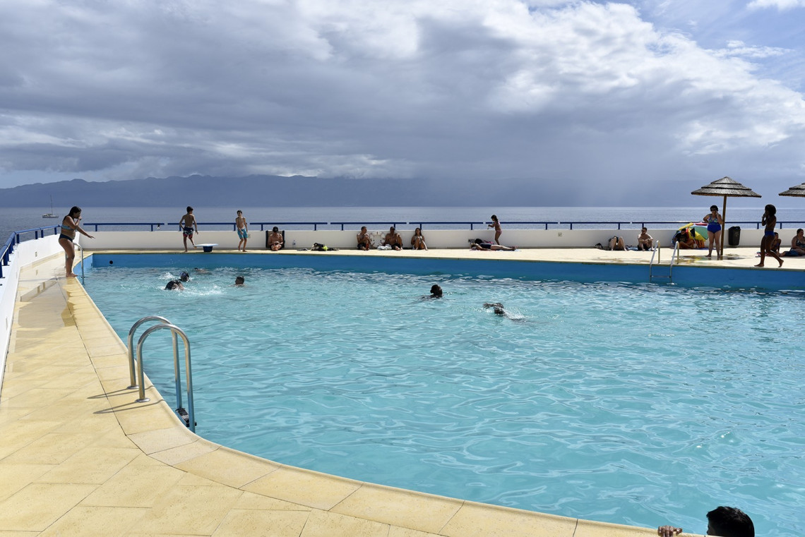 Outdoor seawater swimming pool in Urzelina on S&atilde;o Jorge Island, with visitors relaxing beside the water and views across the Atlantic. Urzelina is known for its oceanfront swimming complex.