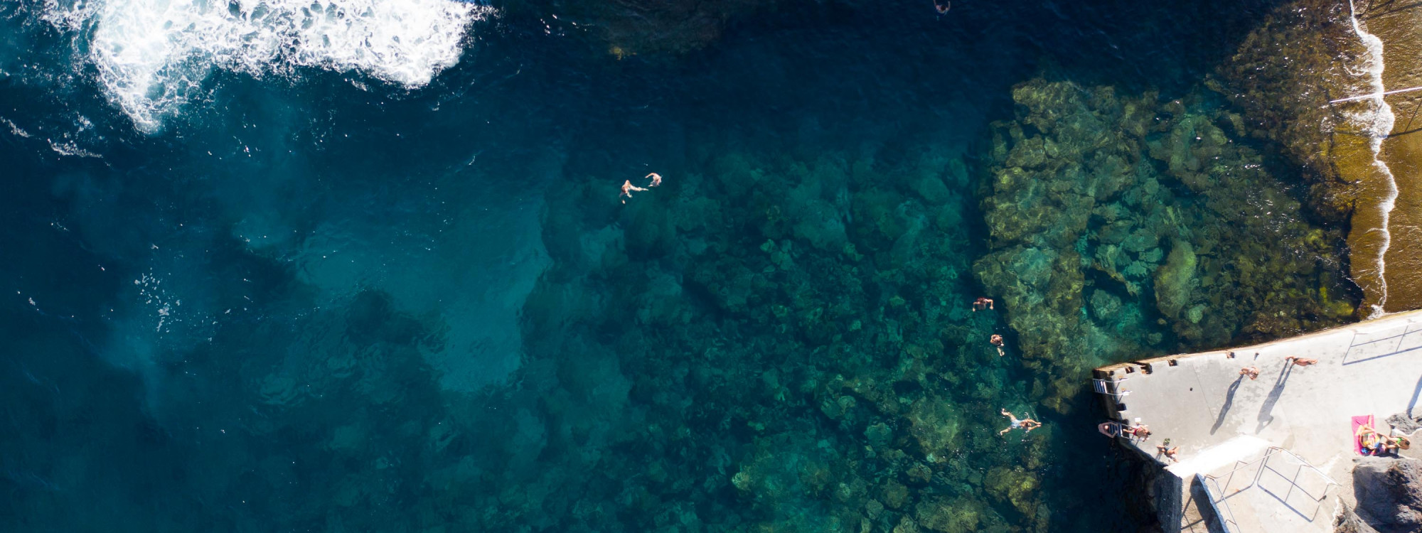 Aerial view of swimmers in the clear Atlantic waters beside the concrete bathing platform at Silveira in Angra do Heroísmo, Terceira Island.