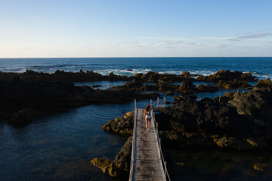 Wooden walkway crossing the Piscinas Naturais dos Biscoitos on Terceira Island, surrounded by black volcanic rocks and natural seawater pools beside the Atlantic Ocean.