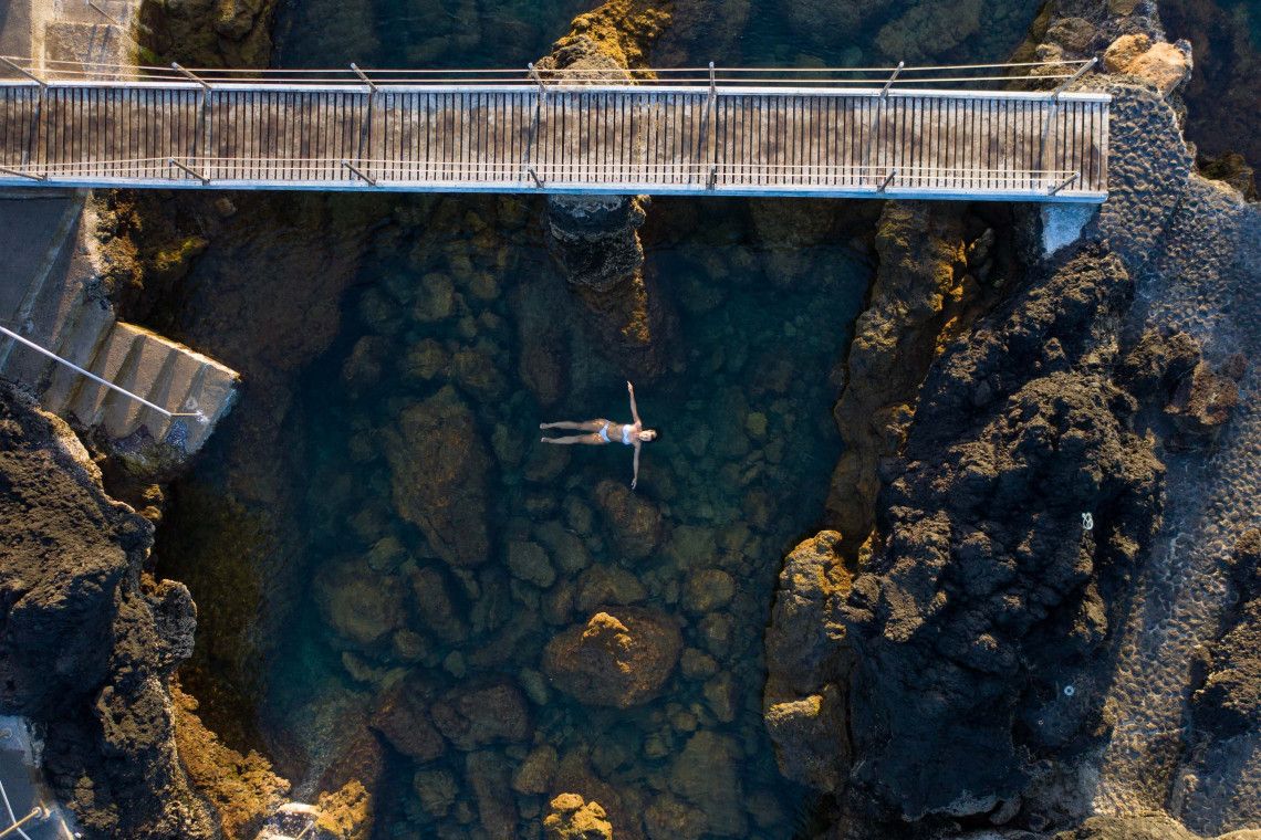 Wooden walkway crossing the Piscinas Naturais dos Biscoitos on Terceira Island, surrounded by black volcanic rocks and natural seawater pools beside the Atlantic Ocean.