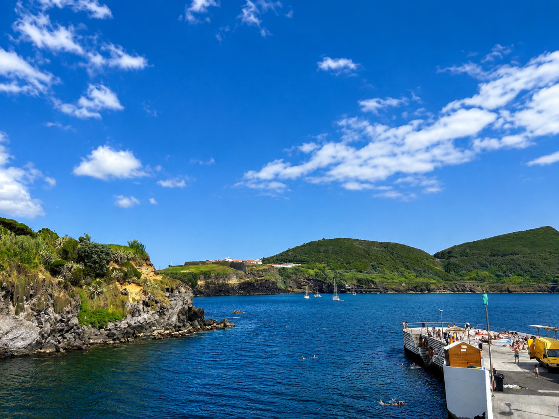 Clear blue Atlantic waters at the Silveira bathing area in Angra do Hero&iacute;smo, with swimmers, a concrete sunbathing platform and green volcanic hills surrounding the bay.