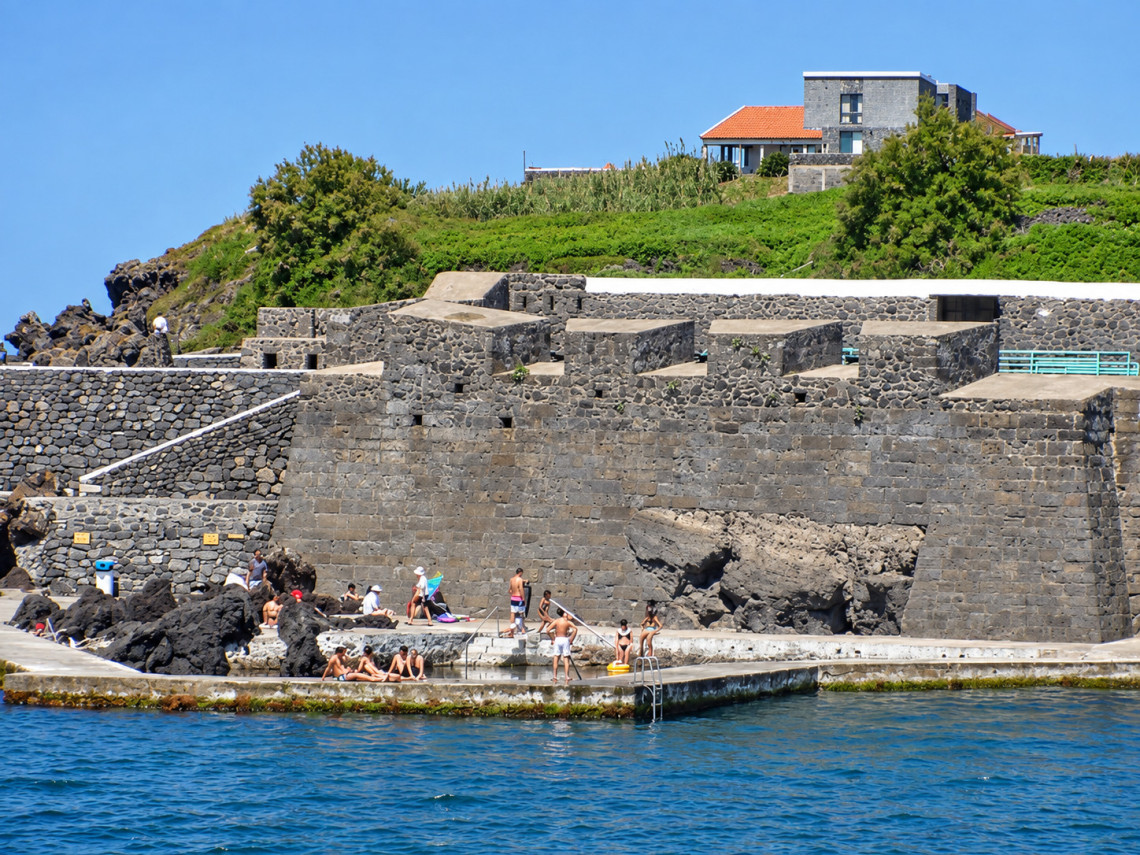 Swimmers enjoying the Zona Balnear do Negrito beside the historic Forte do Negrito in S&atilde;o Mateus da Calheta, Terceira Island, with dark basalt walls rising above the Atlantic swimming area