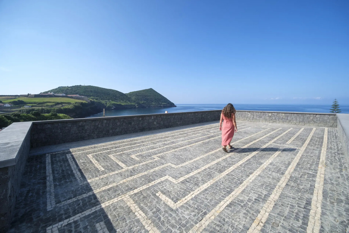 Outdoor terrace at Azores Book Hotel in Angra do Hero&iacute;smo, featuring patterned stone paving and open views toward the Atlantic Ocean and the surrounding volcanic landscape of Terceira Island.