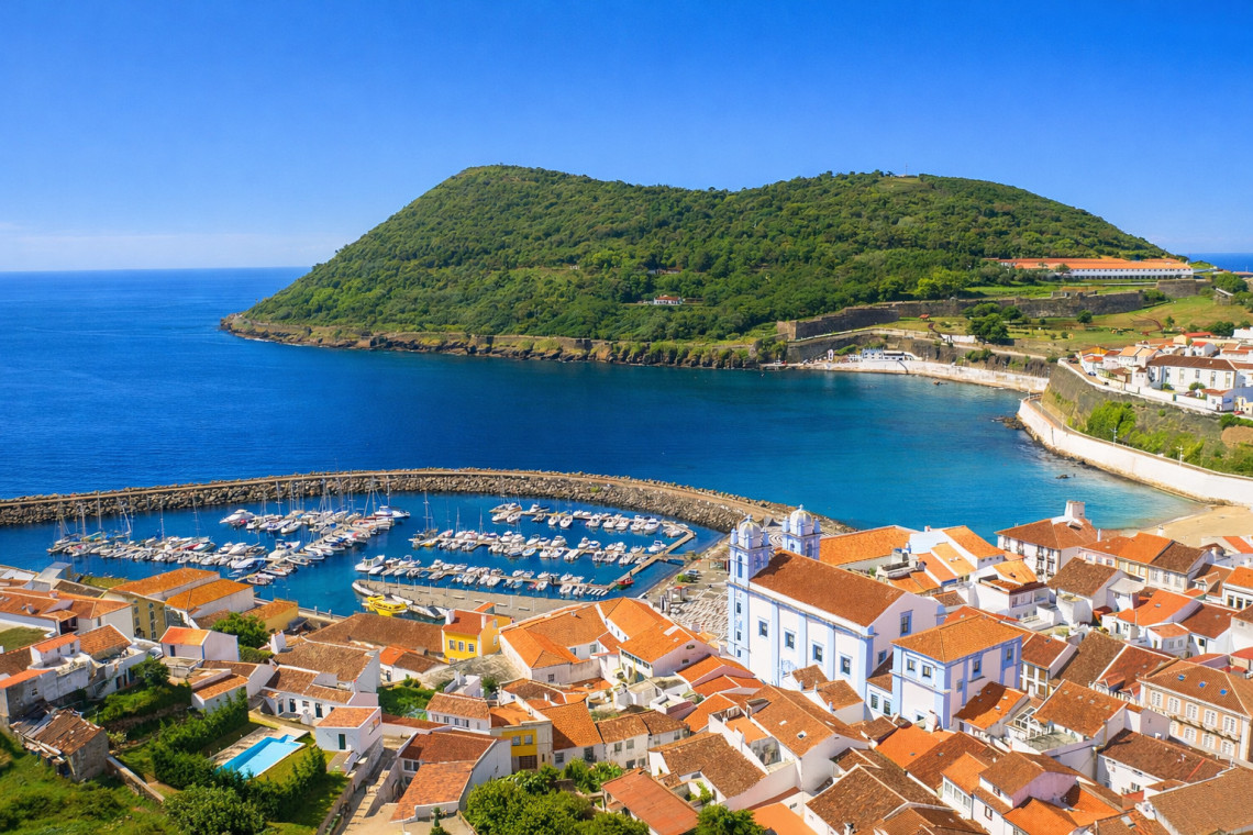 Elevated view over Angra do Hero&iacute;smo on Terceira Island, showing the marina, red-tiled historic center and Igreja da Miseric&oacute;rdia beside the sheltered bay, with Monte Brasil rising beyond.