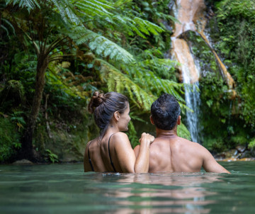 Couple se relaxant dans un bassin thermal naturel de Caldeira Velha avec cascade et végétation tropicale à São Miguel