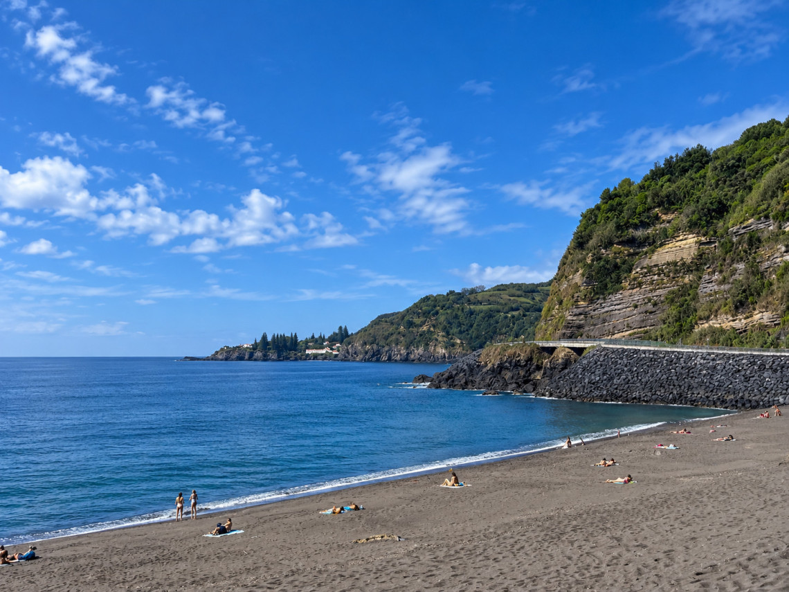 Praia de &Aacute;gua d&rsquo;Alto on the south coast of S&atilde;o Miguel Island, with dark sand, clear Atlantic water and steep green coastal slopes framing the beach.
