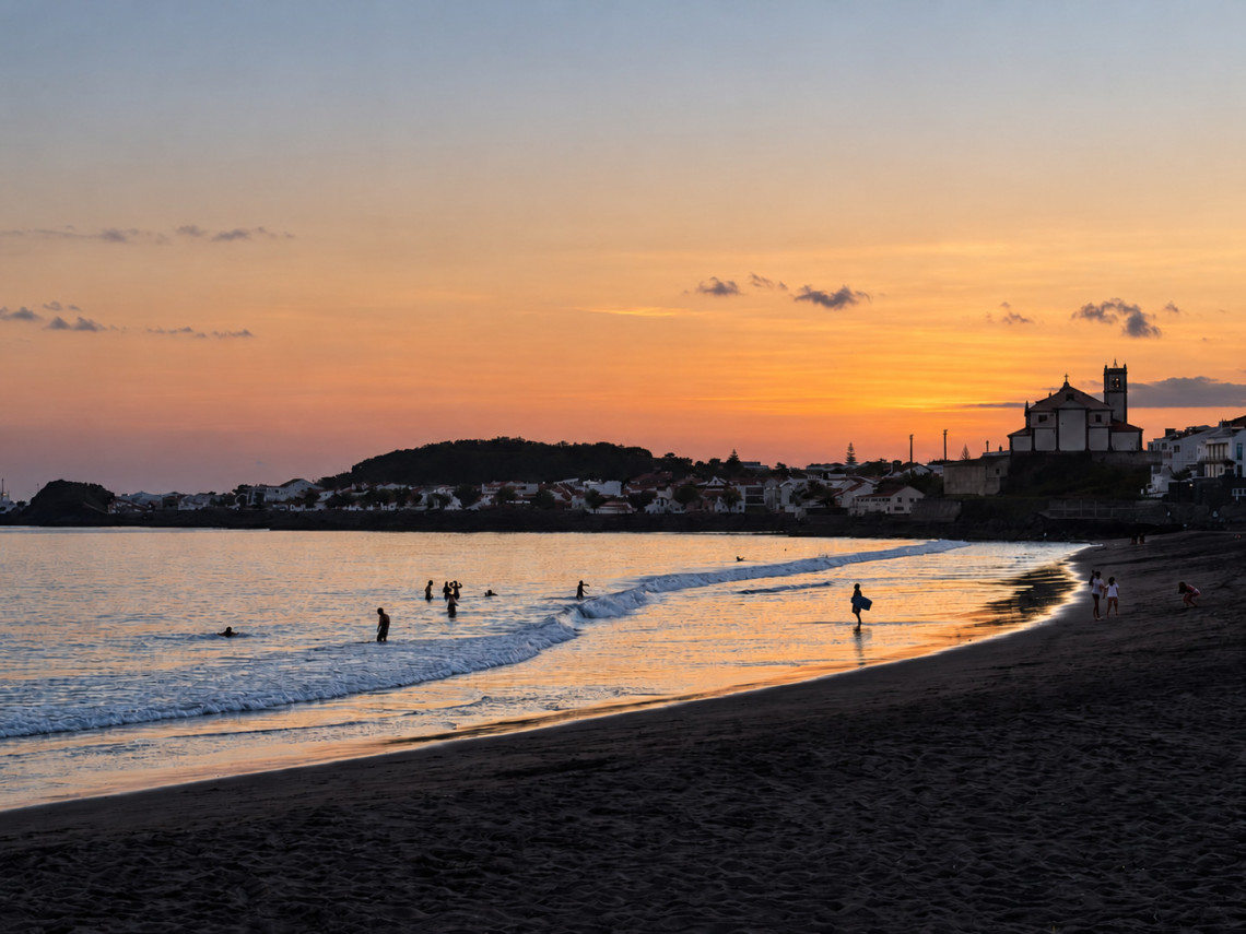 Sunset at Praia das Mil&iacute;cias in Ponta Delgada, S&atilde;o Miguel Island, with swimmers in the Atlantic Ocean, dark volcanic sand and the coastline glowing in warm evening light.