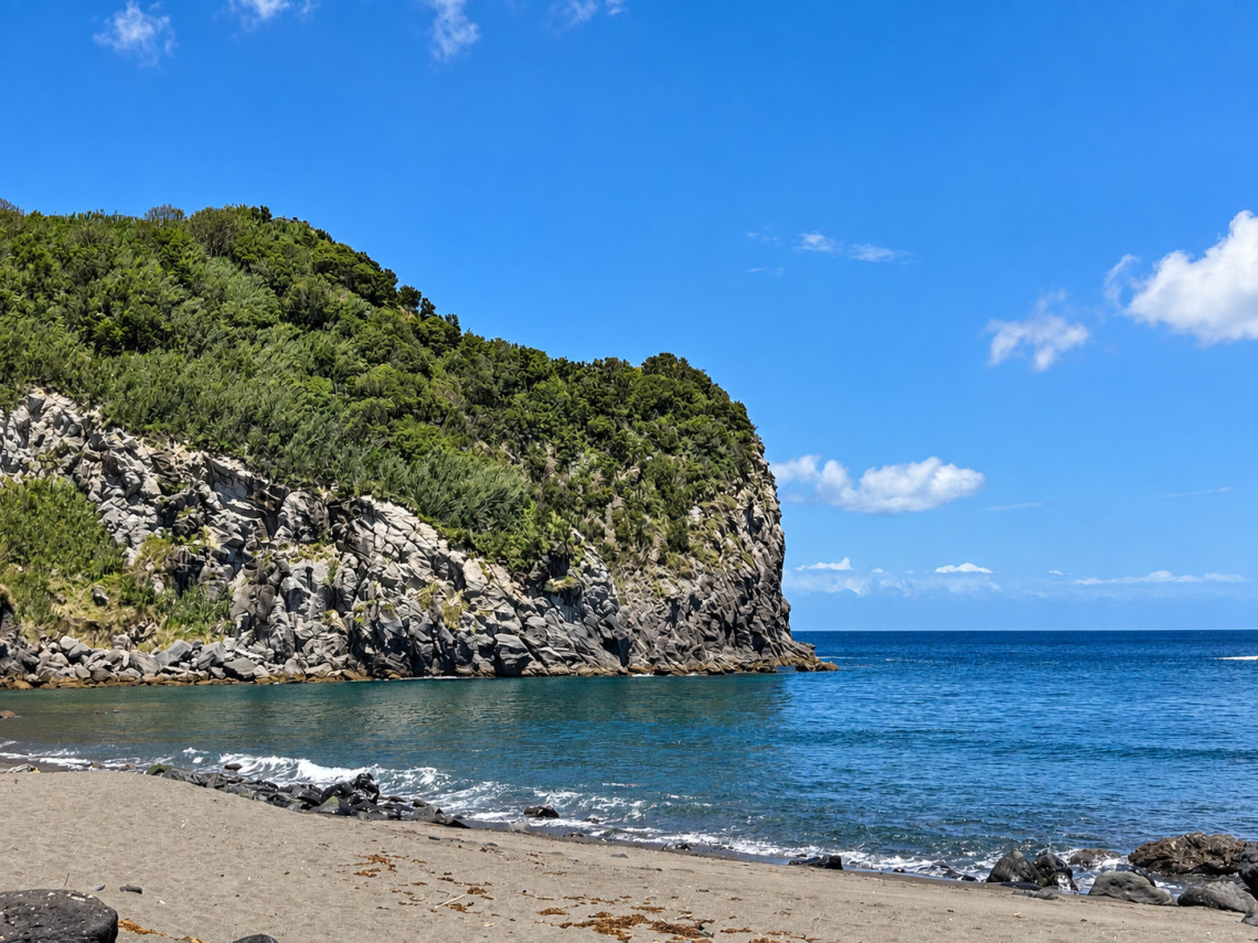 Praia dos Moinhos in Porto Formoso on S&atilde;o Miguel Island, with swimmers and sunbathers along the dark volcanic beach surrounded by steep green coastal cliffs.