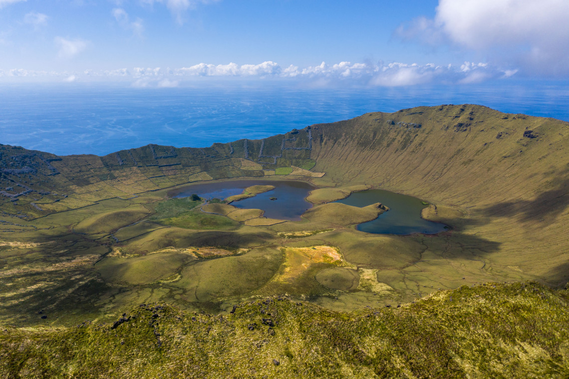 Panoramic view into Caldeir&atilde;o do Corvo on Corvo Island, showing crater lakes, small volcanic cones and green pastureland enclosed by the caldera walls.