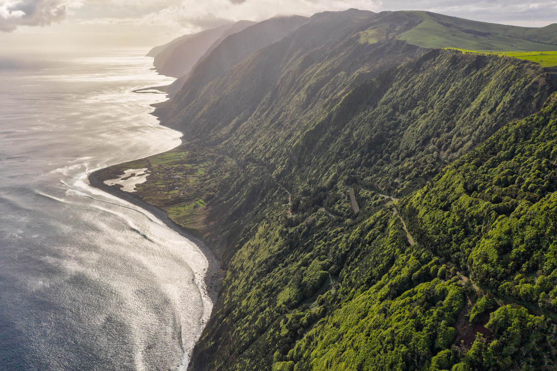 Aerial view along the northern coast of S&atilde;o Jorge Island, showing steep forested volcanic cliffs descending toward coastal faj&atilde;s and the Atlantic Ocean.
