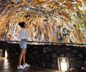 Traveler observing the mineral-rich walls and silica formations inside Algar do Carvão on Terceira Island. The volcanic chimney is known for its distinctive rock textures and naturally formed silica deposits.