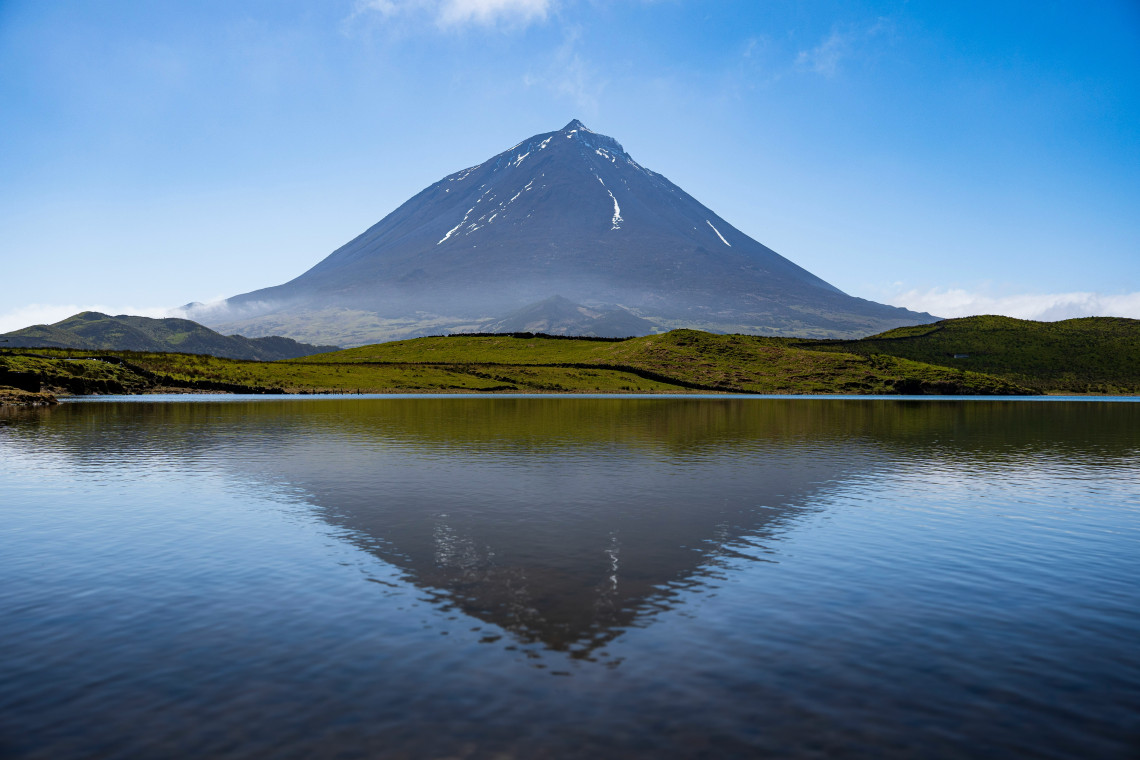 Mount Pico reflected in the calm waters of Lagoa do Capit&atilde;o on Pico Island, with green volcanic terrain surrounding the lagoon.