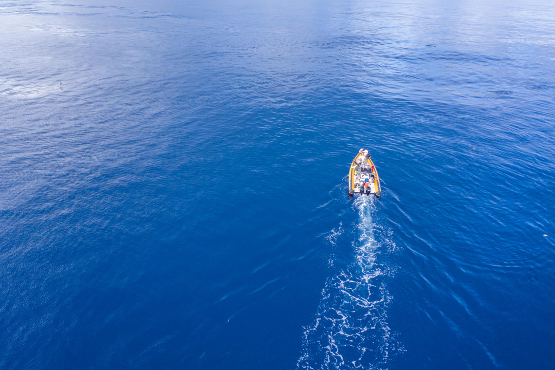 Aerial view of a small whale-watching boat traveling across the deep blue Atlantic Ocean off S&atilde;o Miguel Island, leaving a white wake behind it.