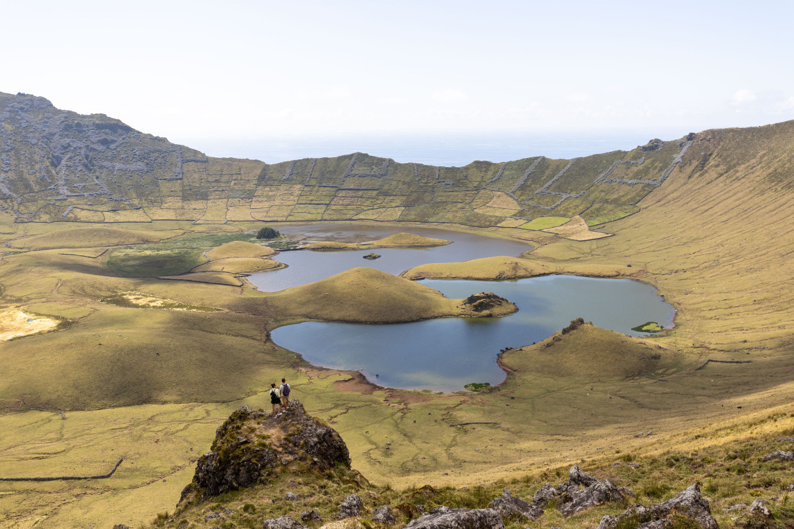 Panoramic view into Caldeir&atilde;o Crater on Corvo Island, Azores, showing shallow lakes, green volcanic cones and steep crater walls. The Atlantic Ocean is visible beyond the rim of the caldera.