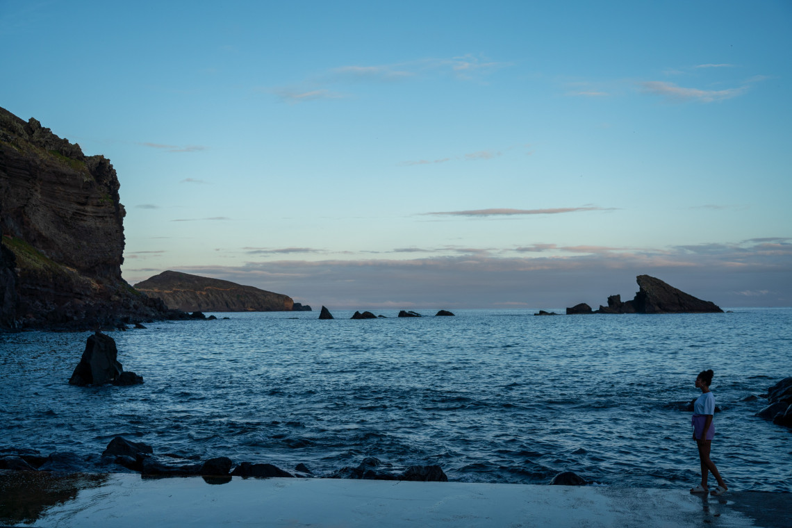 Coastal view of the Carapacho Natural Pools on Graciosa Island, with dark volcanic rocks and calm seawater surrounded by the Atlantic coastline.