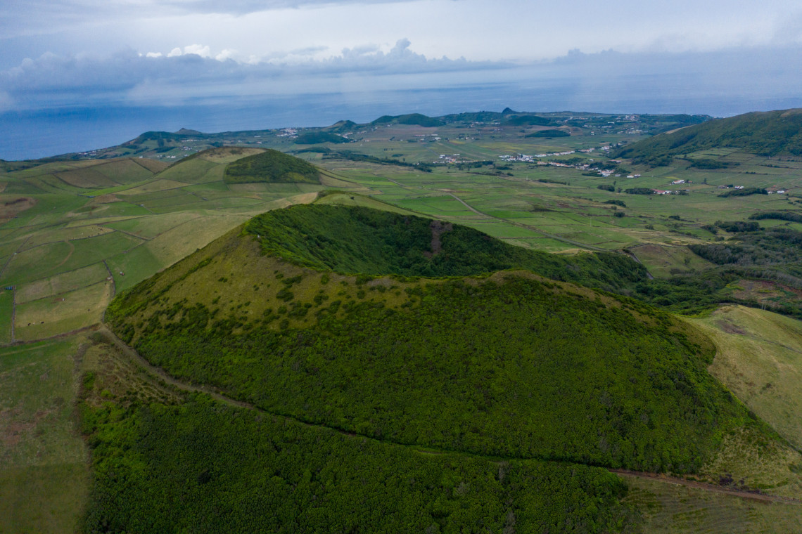 Aerial view of Caldeira da Graciosa, showing its forested volcanic crater surrounded by pastureland, agricultural fields and the Atlantic Ocean.