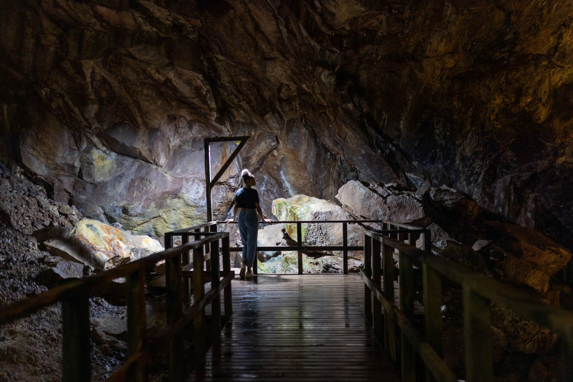 Traveler exploring the vast interior of Furna do Enxofre on Graciosa Island, surrounded by dark volcanic rock illuminated by natural light entering the cave.