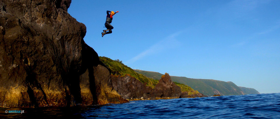 Coasteering participant jumping from a volcanic sea cliff into the Atlantic Ocean along the rugged coast of S&atilde;o Jorge Island.