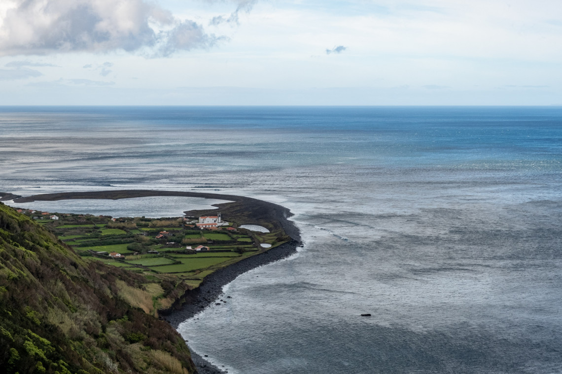 Elevated view of Faj&atilde; da Caldeira de Santo Cristo on S&atilde;o Jorge Island, showing its lagoon, agricultural fields and dark volcanic shoreline beside the Atlantic Ocean.