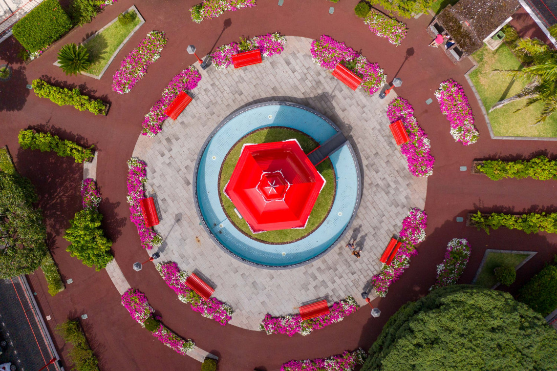 Top-down aerial view of Jardim da Rep&uacute;blica in Velas, S&atilde;o Jorge, showing its red central bandstand, circular paths, flower beds and matching benches.