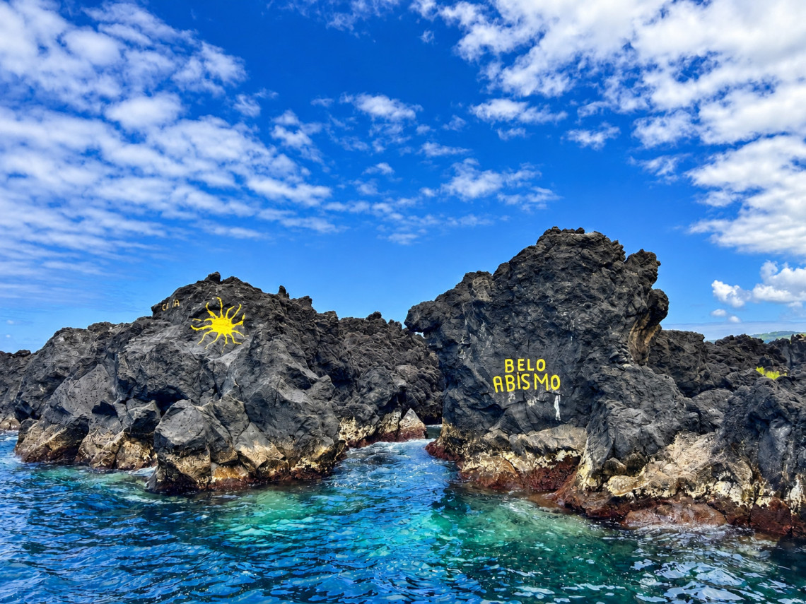 Dark basalt formations at the Biscoitos Natural Pools on Terceira Island, surrounded by clear blue Atlantic water and marked with the local Belo Abismo inscription.