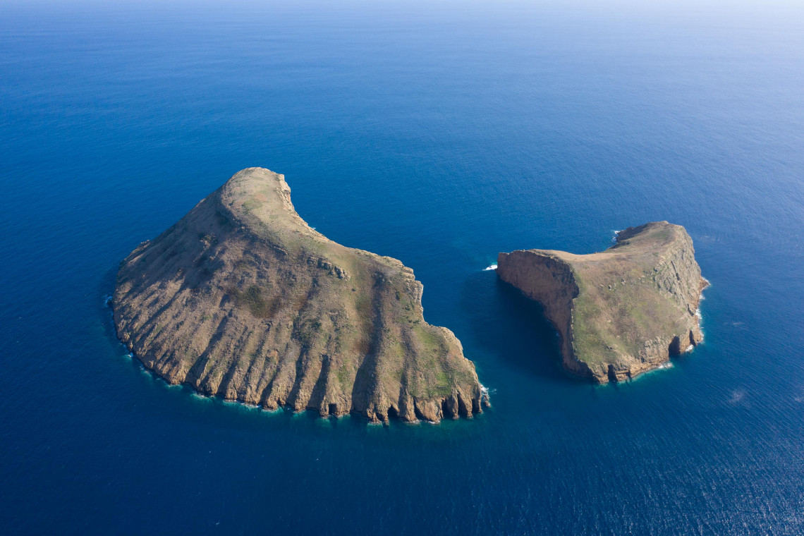 Aerial view of Ilh&eacute;us das Cabras off the southern coast of Terceira Island, showing two steep volcanic islets surrounded by deep blue Atlantic water.
