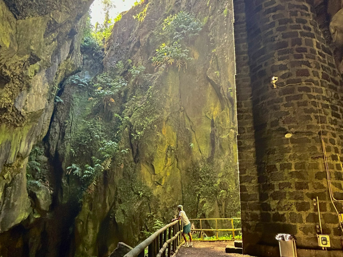 Visitor exploring the entrance area of Furna do Enxofre on Graciosa Island, surrounded by high volcanic rock walls and vegetation beside the stone access tower.