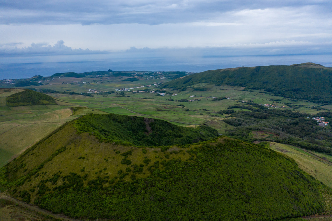 Aerial view across the Caldeira da Graciosa, showing a forested volcanic crater surrounded by pastureland, agricultural fields and the Atlantic Ocean.