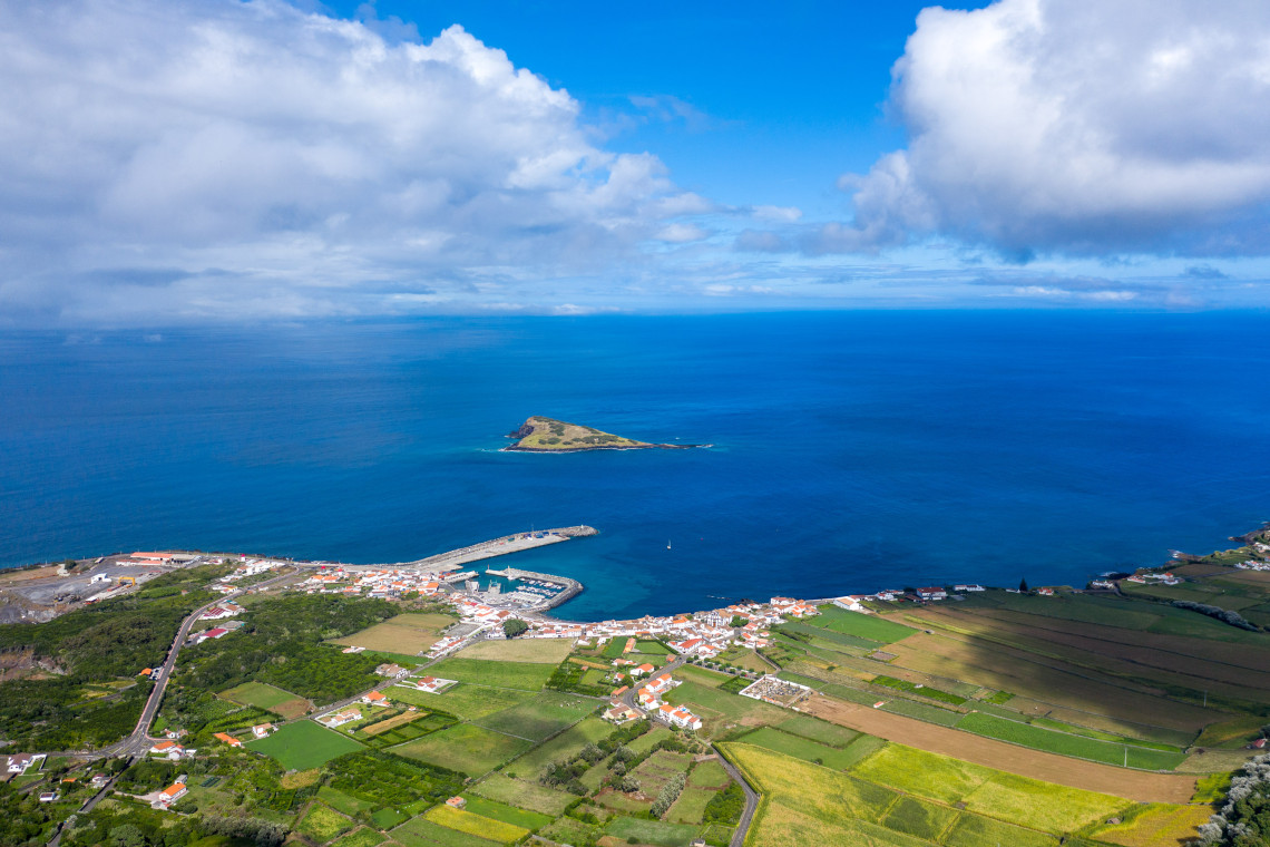 Elevated view over Vila da Praia on Graciosa Island, showing the harbor, whitewashed settlement, agricultural fields and Ilh&eacute;u da Praia offshore.