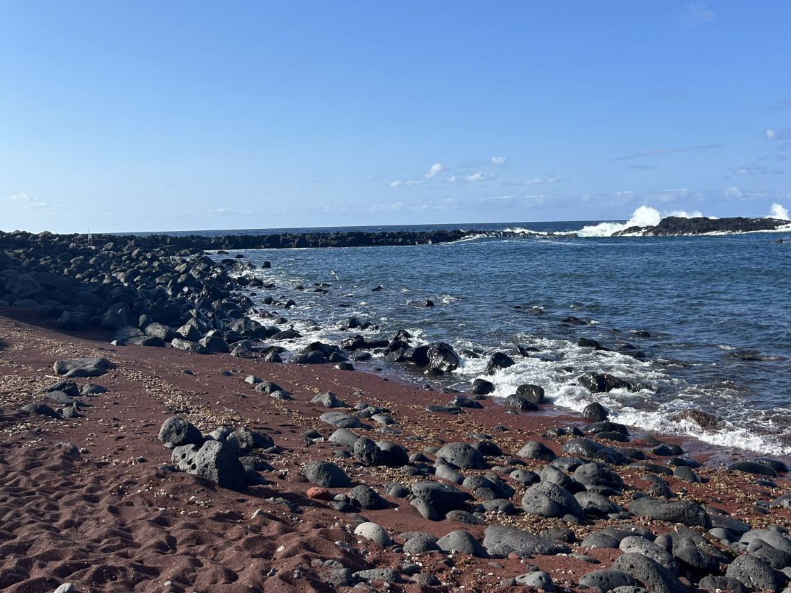 Barro Vermelho Beach on Graciosa Island, with reddish volcanic sand, rounded dark basalt stones and Atlantic waves breaking along the shore.