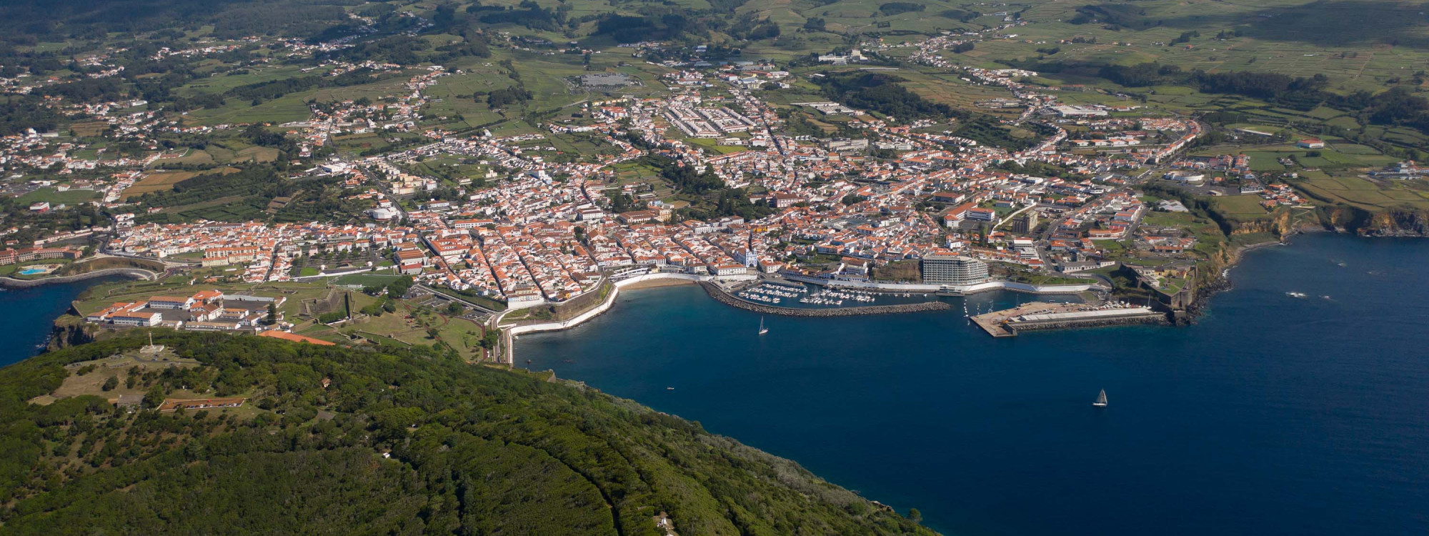 Aerial view of Praia da Vitória on Terceira Island, showing the curved bay, sandy beach, marina and dense town center surrounded by green countryside.