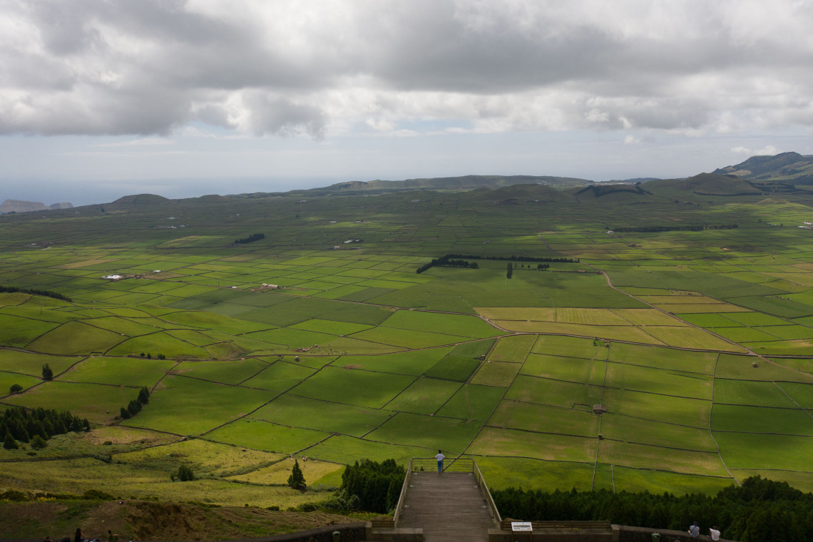 Panoramic view from Serra do Cume on Terceira Island, showing a geometric patchwork of green agricultural fields divided by stone walls across the volcanic plain.