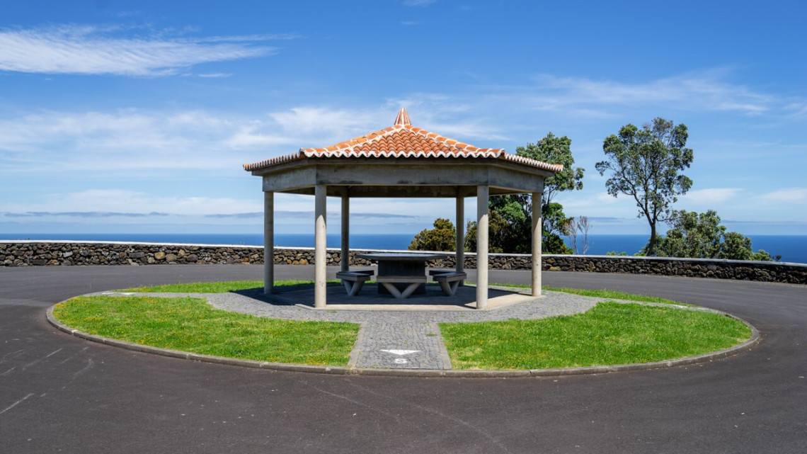 Tiled-roof picnic shelter at Miradouro do Raminho on the northern coast of Terceira Island, with stone walls framing an open view across the Atlantic Ocean.