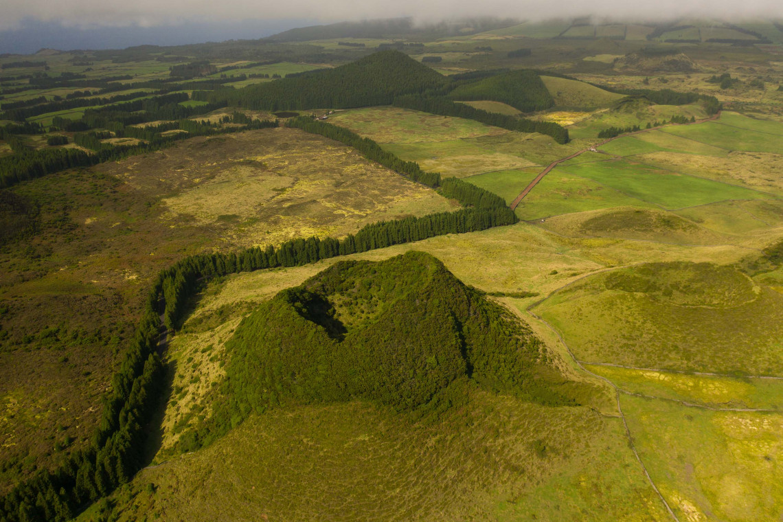 Aerial view of Pico Gaspar in the interior of Terceira Island, showing its vegetation-covered volcanic cone and crater surrounded by highland pasture and forest.