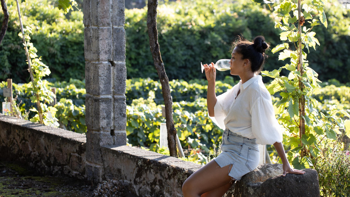 Traveler tasting local wine among the vineyards of Biscoitos on Terceira Island, where vines are traditionally cultivated within volcanic-stone enclosures.