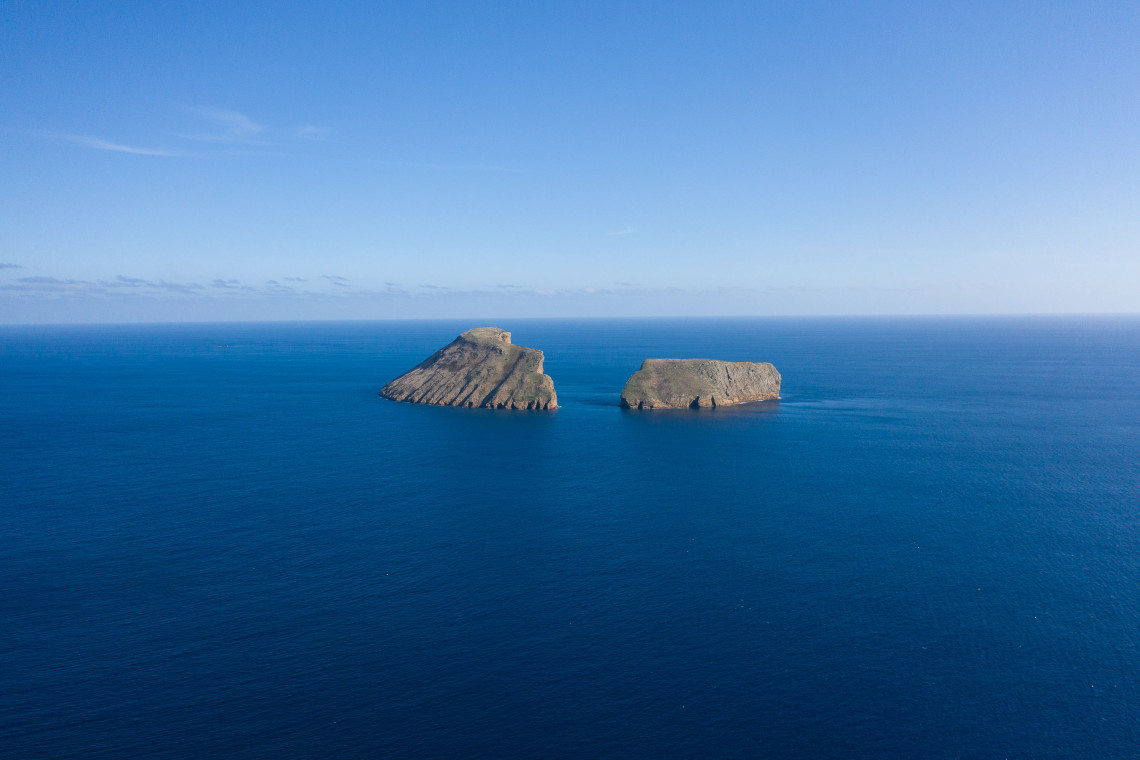 Aerial view of the two Ilh&eacute;us das Cabras off the southern coast of Terceira Island, with their steep volcanic cliffs rising from the deep blue Atlantic Ocean.