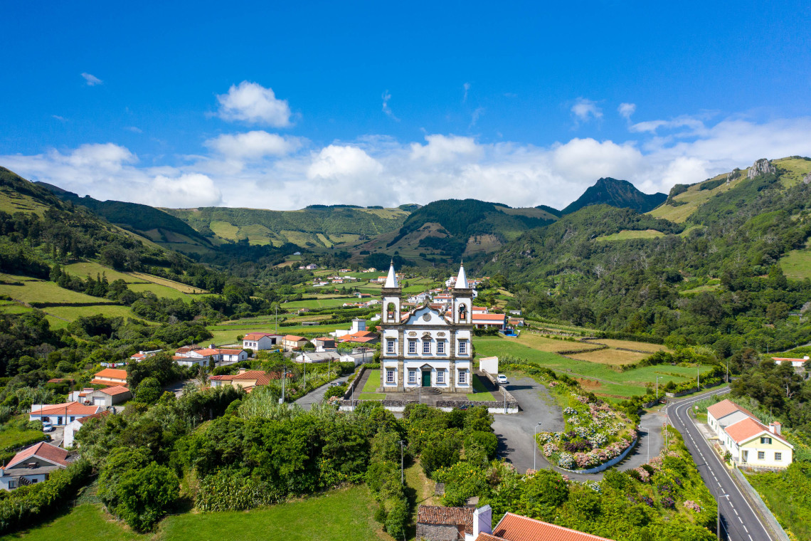 Nossa Senhora de Lourdes Church stands in Fazenda de Santa Cruz on Flores Island in the Azores, Portugal. Its white fa&ccedil;ade and twin bell towers are surrounded by farmland, red-roofed houses and steep green volcanic hills.