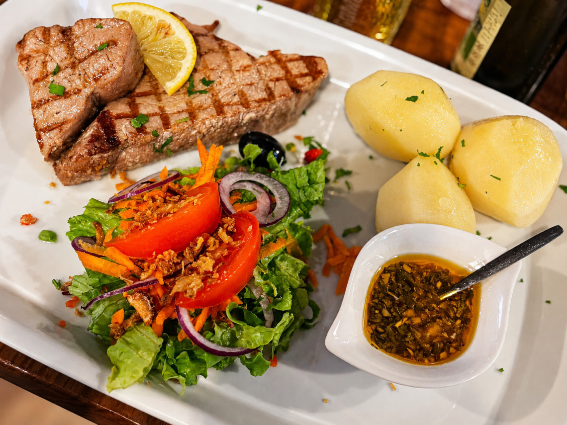 Grilled tuna steaks served with boiled potatoes, fresh salad, lemon and a seasoned olive oil sauce on Pico Island. The dish reflects the seafood-focused cuisine of the Azores.