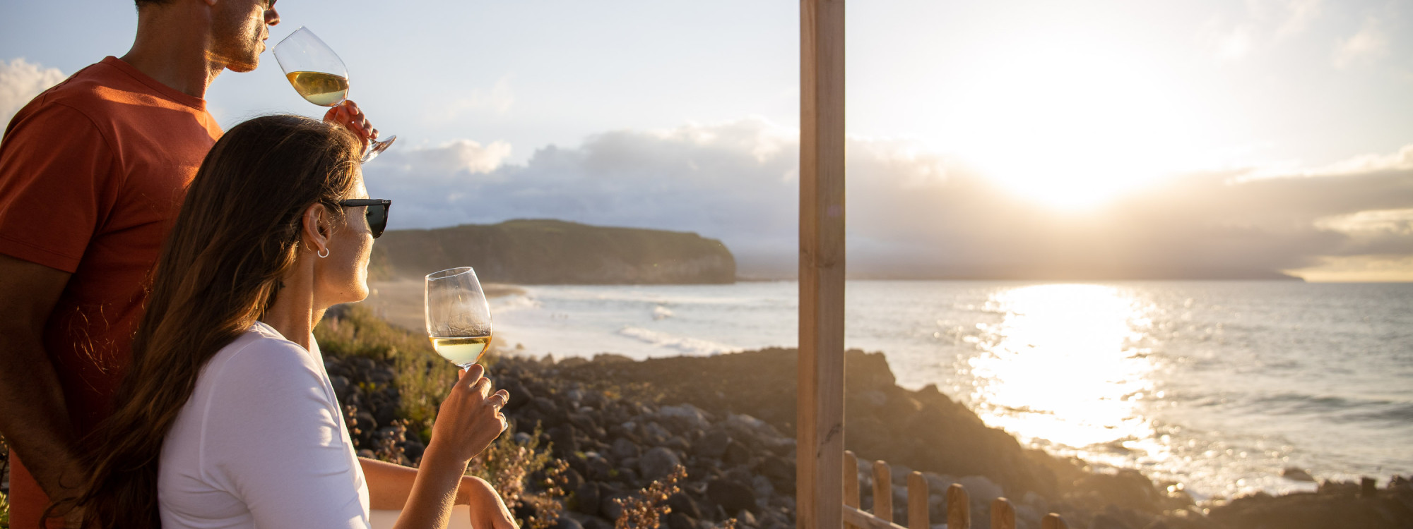 Couple enjoying glasses of wine overlooking Areal de Santa Bárbara in Ribeira Grande, with the Atlantic Ocean glowing in the evening sunlight.