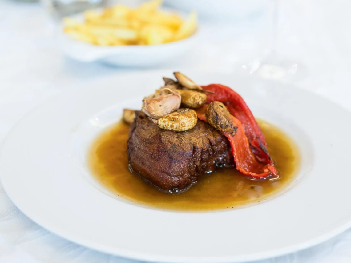 Traditional Azorean beef steak served with garlic and roasted red pepper in a rich sauce, accompanied by fries in the background.