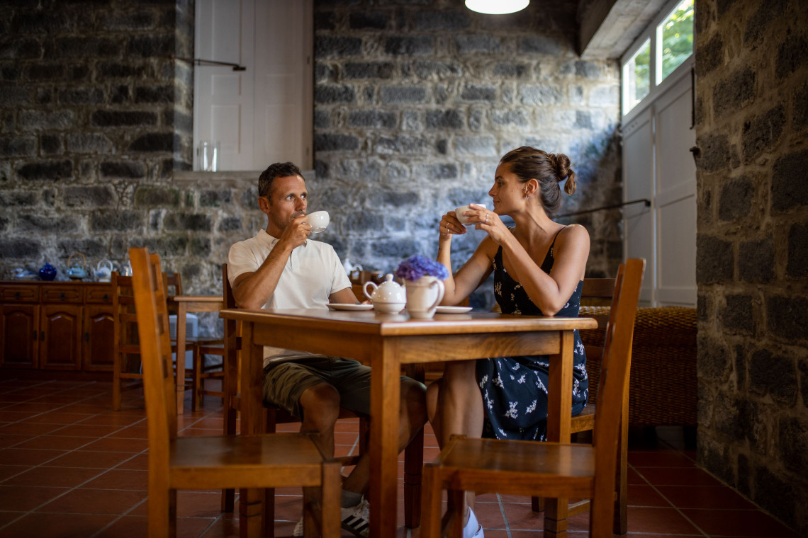 Couple drinking tea inside the Gorreana Tea Plantation on S&atilde;o Miguel Island, seated in a traditional stone-walled interior.