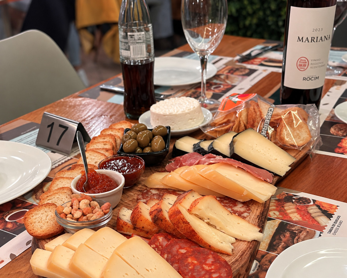 Selection of Azorean cheeses, cured meats, olives, bread and preserves arranged on a tasting board with wine.