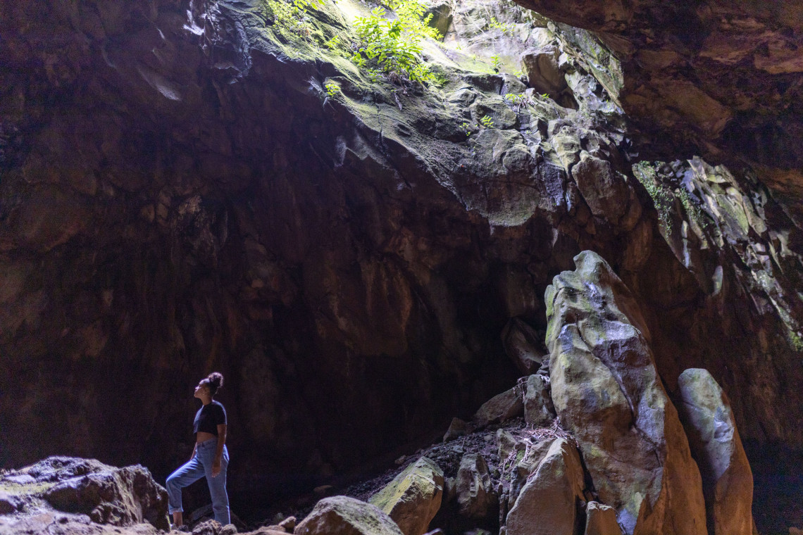 Traveler exploring the vast interior of Furna do Enxofre on Graciosa Island, surrounded by dark volcanic rock illuminated by natural light entering the cave.