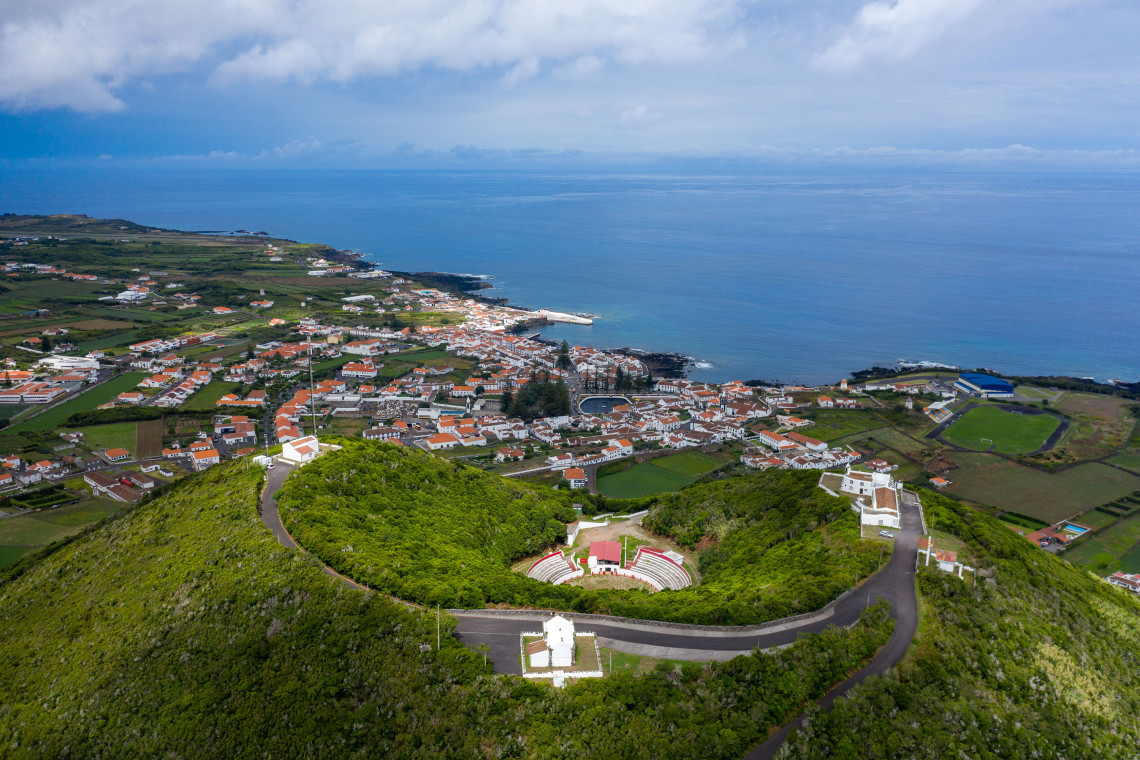 Aerial view over Santa Cruz da Graciosa, with white houses and red roofs extending toward the Atlantic coast and the Pra&ccedil;a de Touros da Graciosa visible on Monte de Nossa Senhora da Ajuda.
