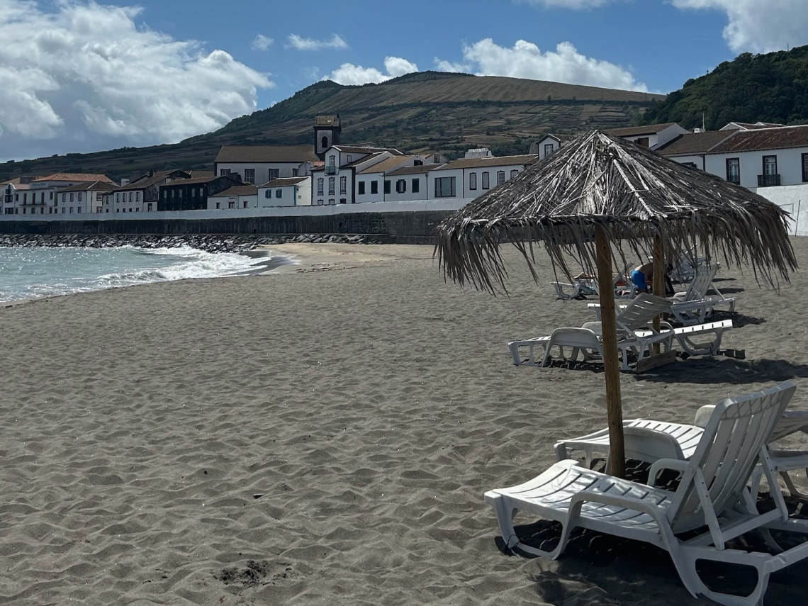 Praia de S&atilde;o Mateus on Graciosa Island, with a sandy shoreline, sun loungers and traditional whitewashed buildings beneath the surrounding volcanic hills. It is Graciosa&rsquo;s only sandy beach.