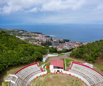 View over the Praça de Touros da Graciosa on Monte de Nossa Senhora da Ajuda, with its curved red-and-white seating overlooking Santa Cruz da Graciosa and the Atlantic Ocean. The arena is set within an extinct volcanic crater.