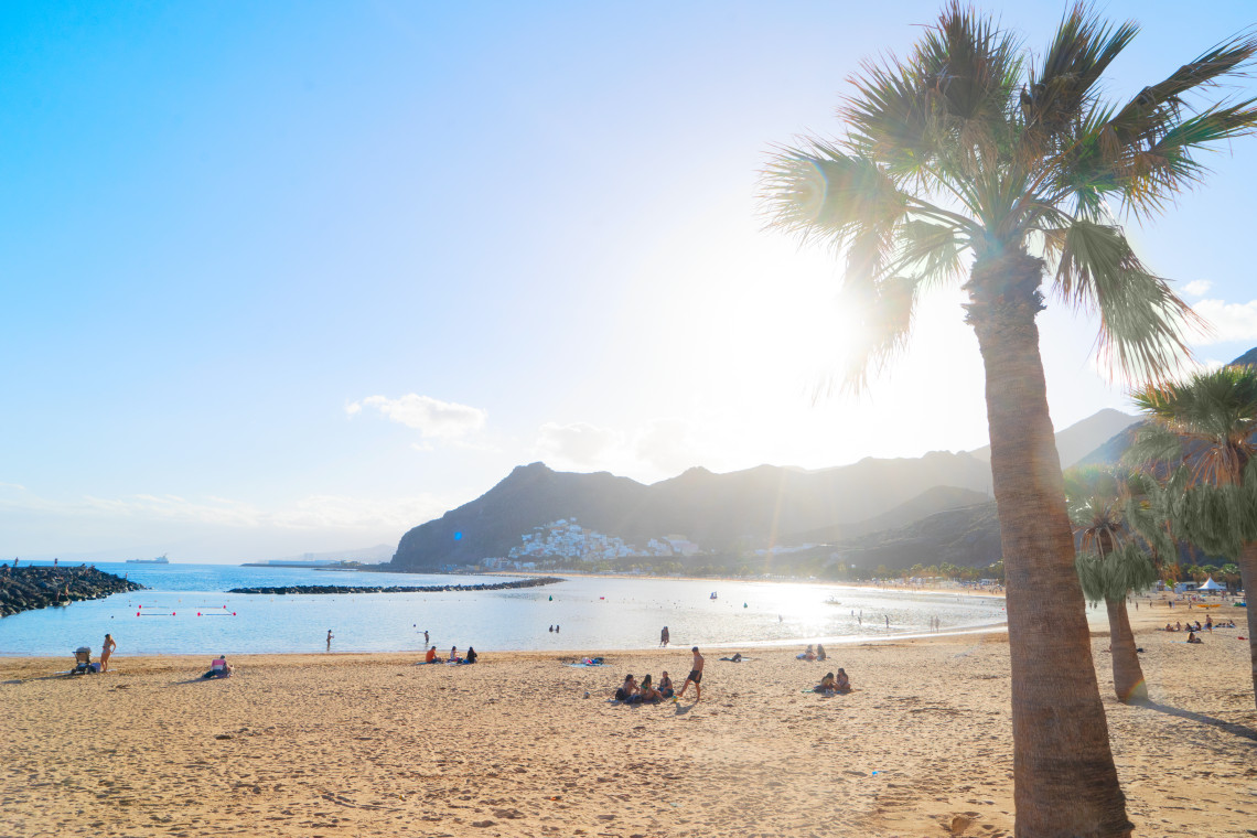 Playa de Las Teresitas near Santa Cruz de Tenerife, with its broad sandy shore, calm Atlantic waters, palm trees, and the rugged Anaga Mountains in the background.